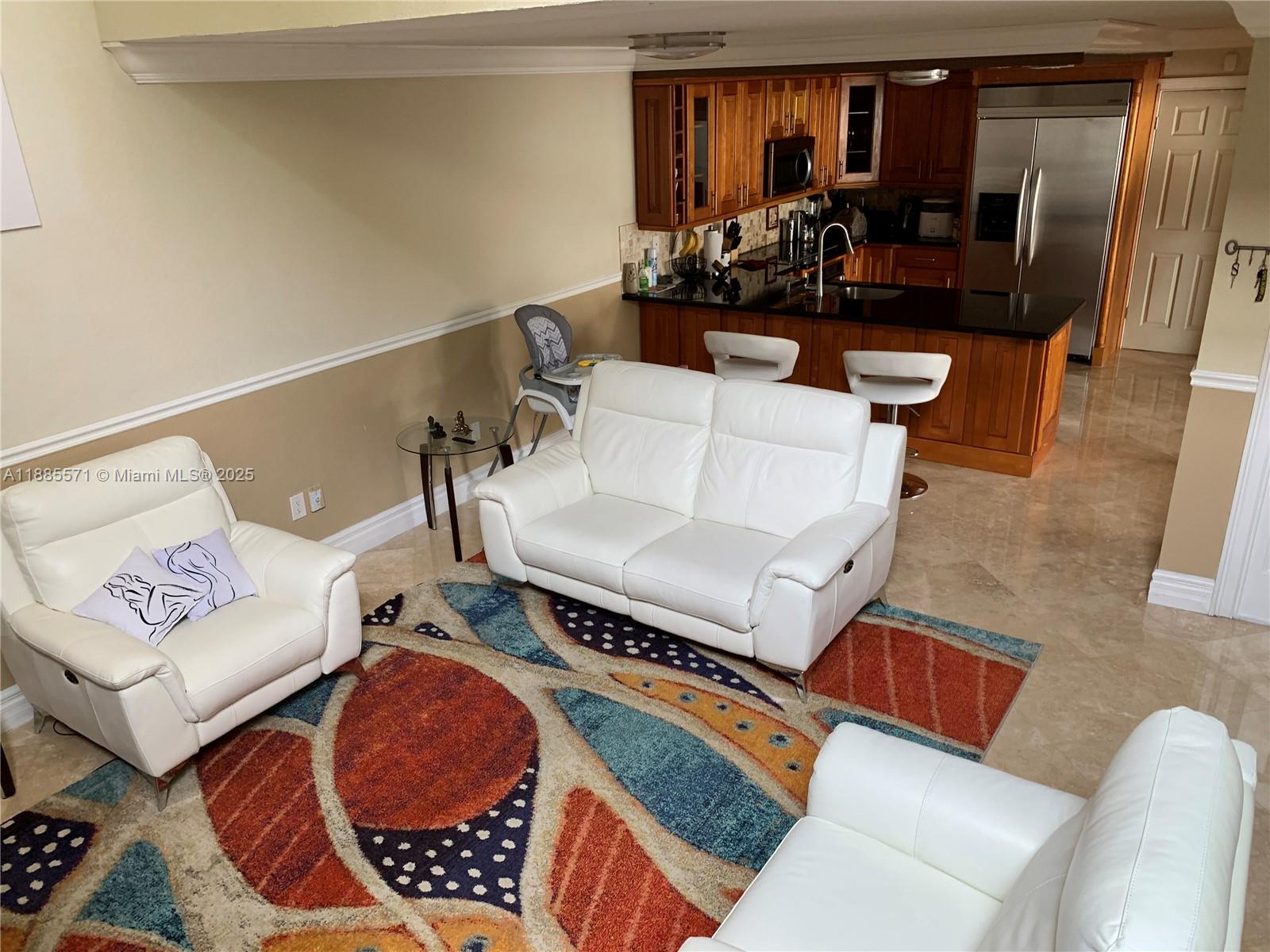 A living room with white leather furniture and a patterned rug opens to a kitchen — 10115 NW 4th Ln # 8, Miami FL 33172, MIAMI, FL