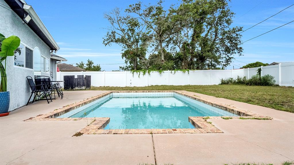 A rectangular swimming pool sits in a backyard with a concrete patio and white fence — 1160 MANITOBA STREET, DELTONA, FL