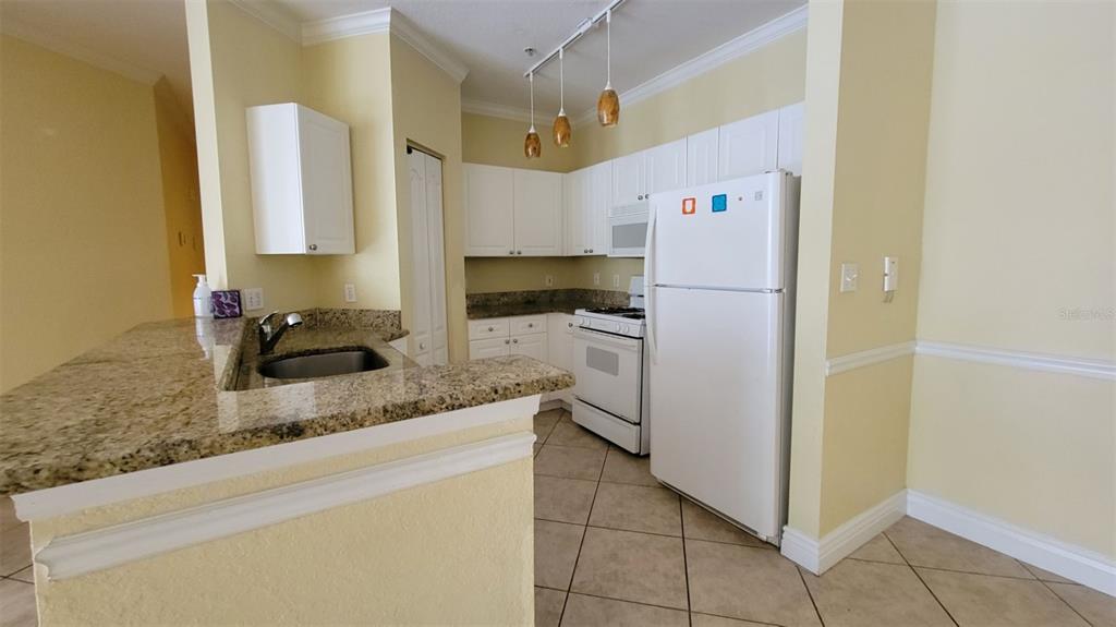 A kitchen features white cabinets, granite countertops, a white refrigerator, and tile flooring — 2713 VIA MURANO UNIT 221, CLEARWATER, FL