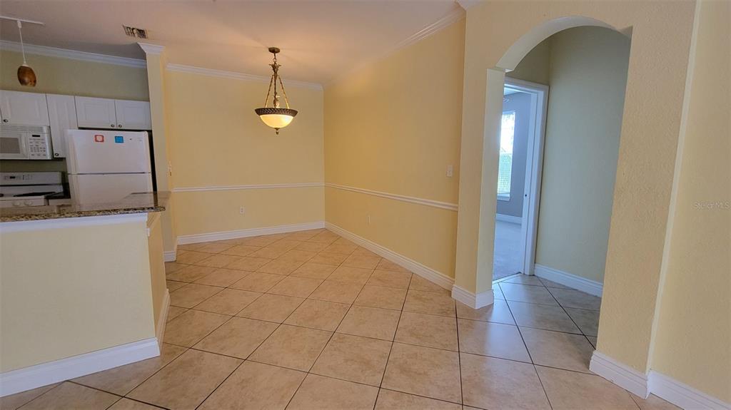 A dining area with tile floors, yellow walls, and a chandelier next to a kitchen — 2713 VIA MURANO UNIT 221, CLEARWATER, FL
