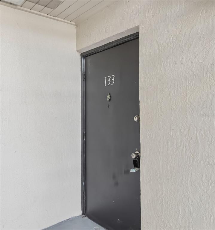 A dark-colored front door marked with the number 133 is set into a textured wall — 2569 N ALAFAYA TRAIL UNIT 133, ORLANDO, FL