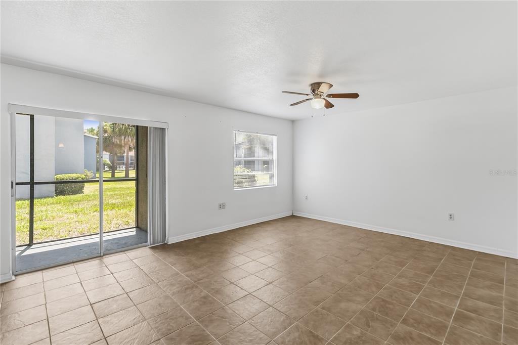 An empty living room features beige tile flooring, white walls, a ceiling fan, and sliding doors — 2569 N ALAFAYA TRAIL UNIT 133, ORLANDO, FL