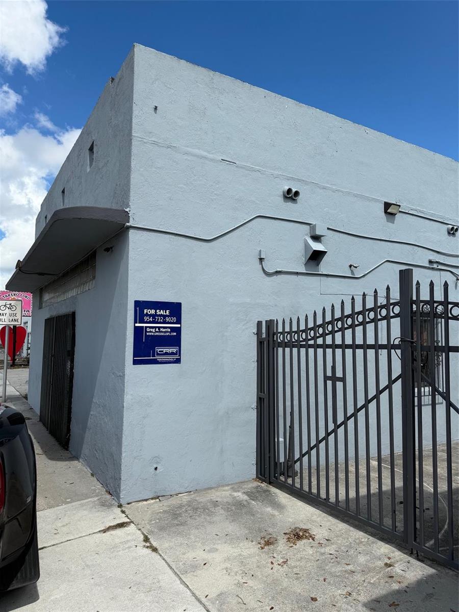 The exterior of a light blue commercial building features a metal gate and for-sale sign — 6815 NW 7th Avenue, Miami FL 33150, MIAMI, FL