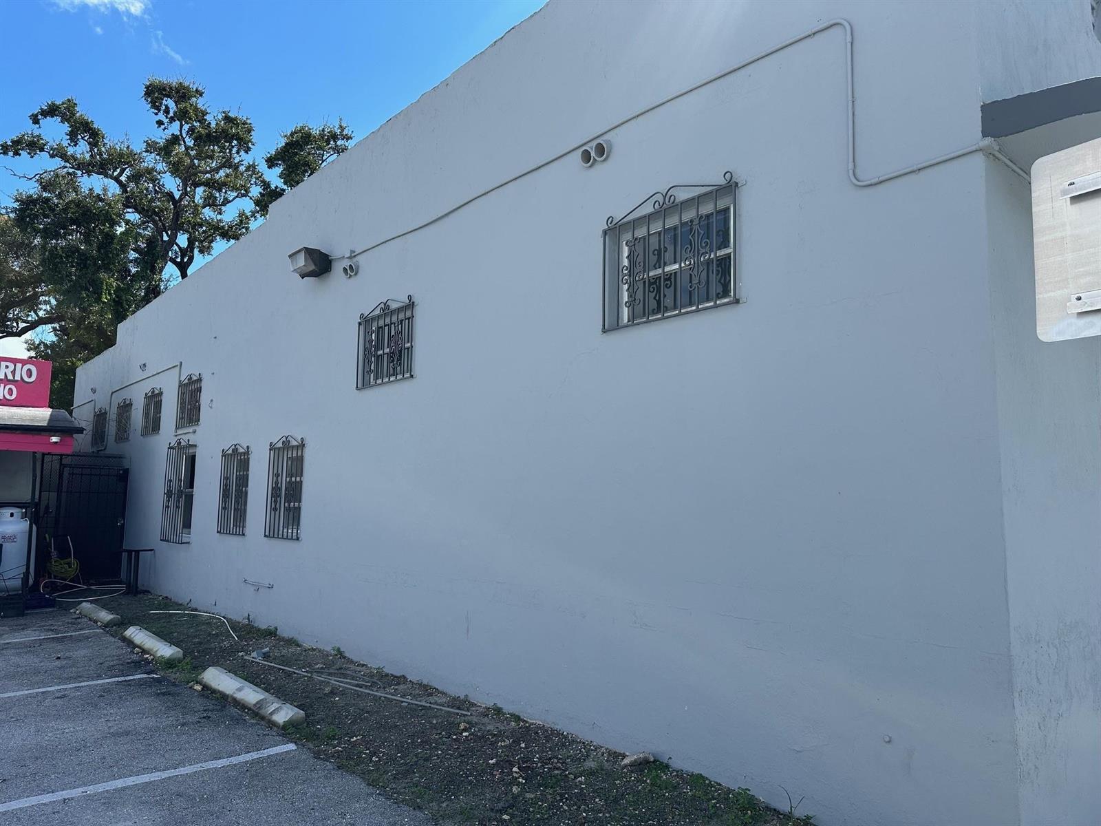 A gray exterior wall of a building features multiple windows with decorative metal security bars — 6815 NW 7th Avenue, Miami FL 33150, MIAMI, FL