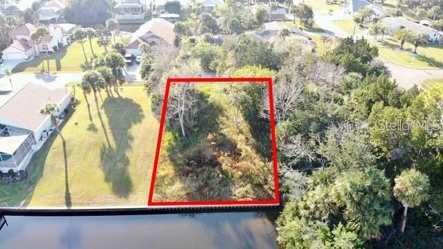 An aerial view shows a vacant, wooded waterfront lot outlined in red next to a house — 5 COLONIA COURT, PALM COAST, FL