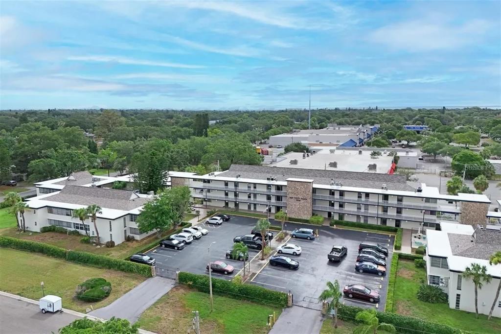 An aerial view shows a multi-story apartment building with a parking lot and surrounding trees — 6100 12TH STREET S UNIT 107, ST PETERSBURG, FL