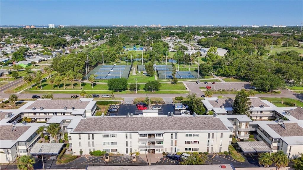 An aerial view shows a multi-story apartment complex situated next to a public tennis court — 6100 12TH STREET S UNIT 107, ST PETERSBURG, FL