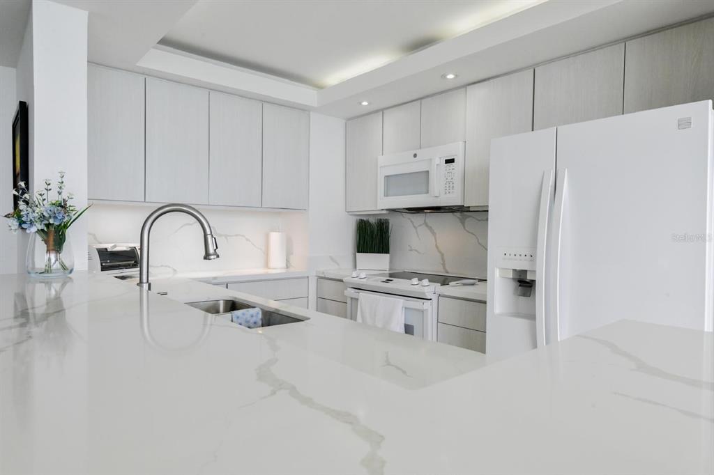 A modern kitchen with white countertops overlooks a dining area and a balcony with ocean views — 4745 ISLA VERDE AVENUE UNIT 17G, CAROLINA, PR
