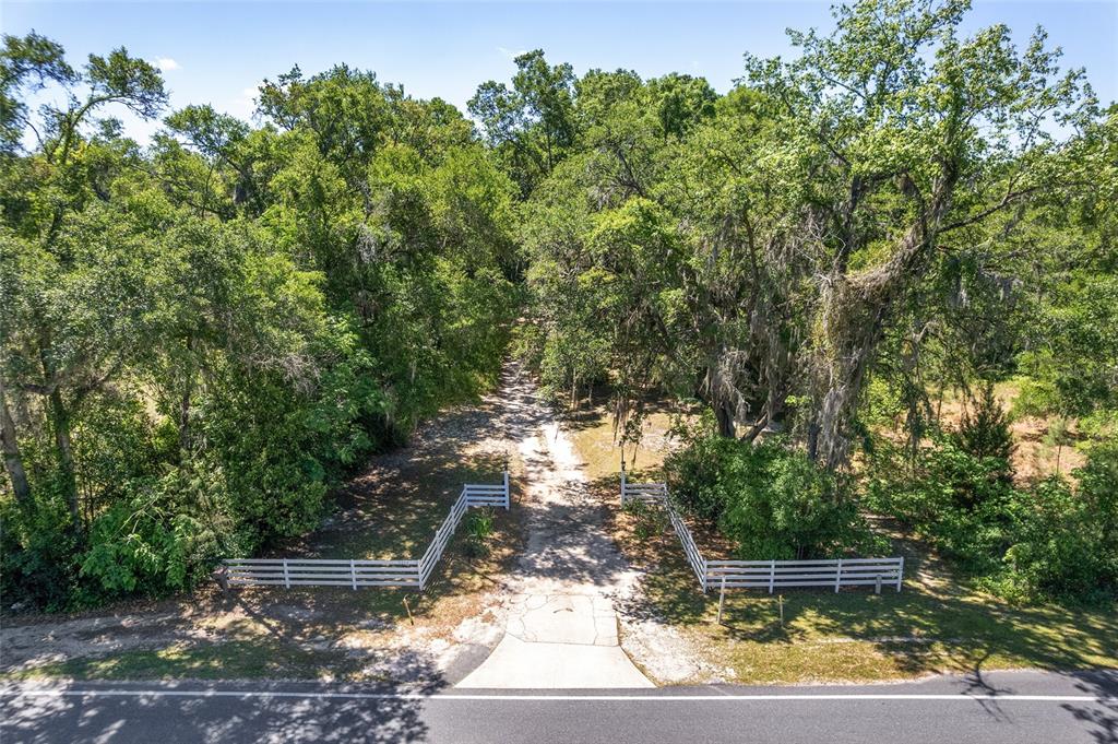 An aerial view shows a white fence marking the entrance to a wooded dirt driveway — 5050 W HIGHWAY 326, OCALA, FL