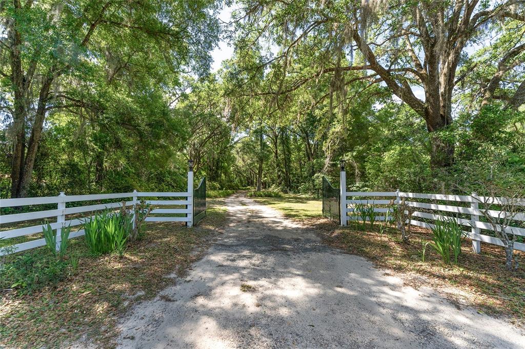 A dirt driveway leads through an open metal gate flanked by white wooden fences — 5050 W HIGHWAY 326, OCALA, FL