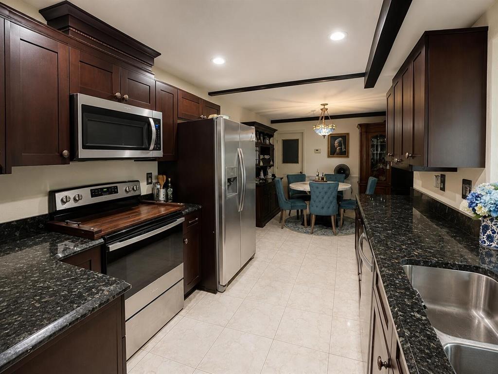 A kitchen with dark wood cabinets, granite countertops, stainless steel appliances, and an adjacent dining area — 7317 LIME TREE COURT, SEBRING, FL