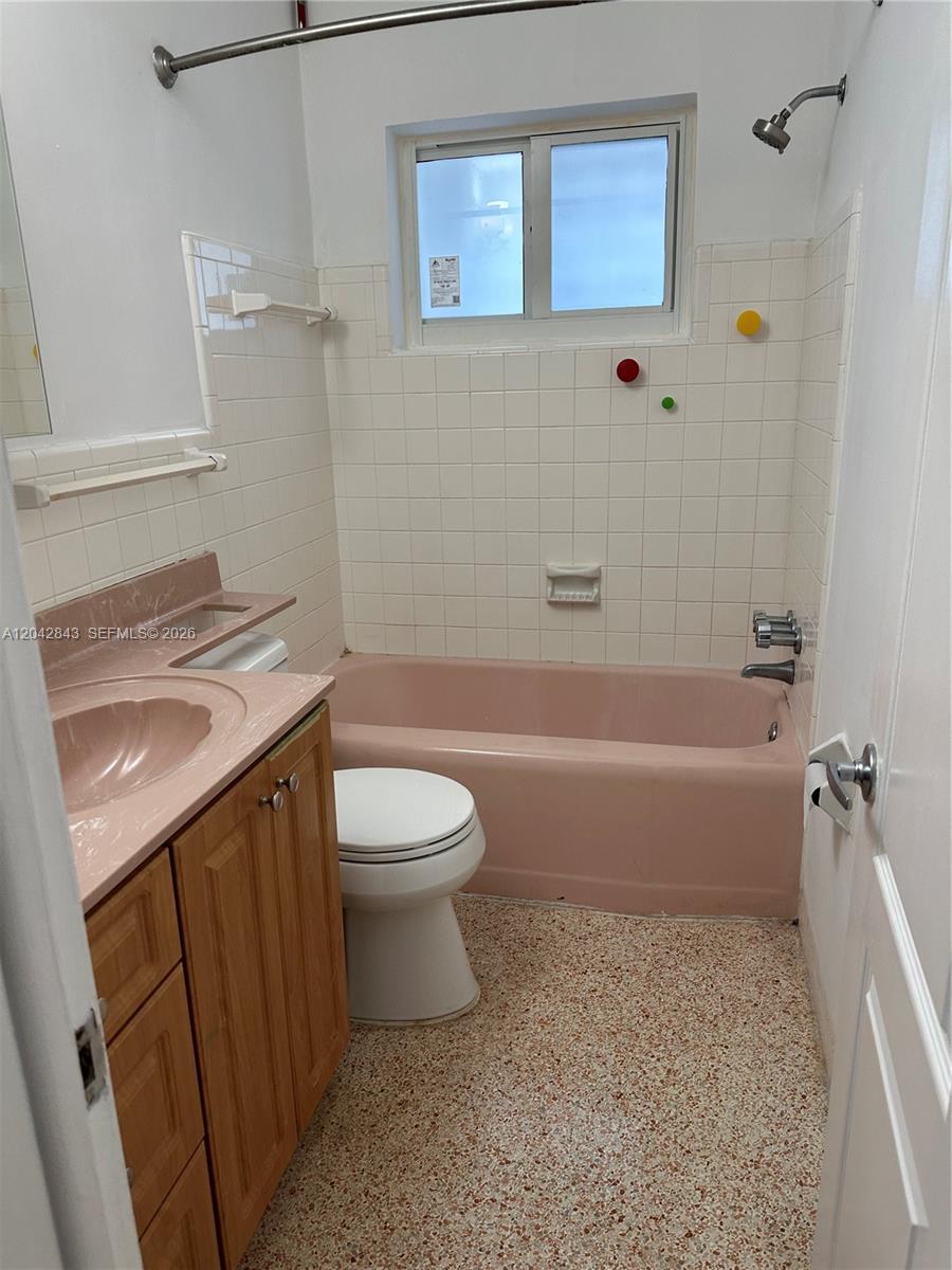 A bathroom features a pink bathtub and vanity, white tiled walls, and speckled flooring — 7931 SW 13th Ter # 7931, Miami FL 33144, MIAMI, FL