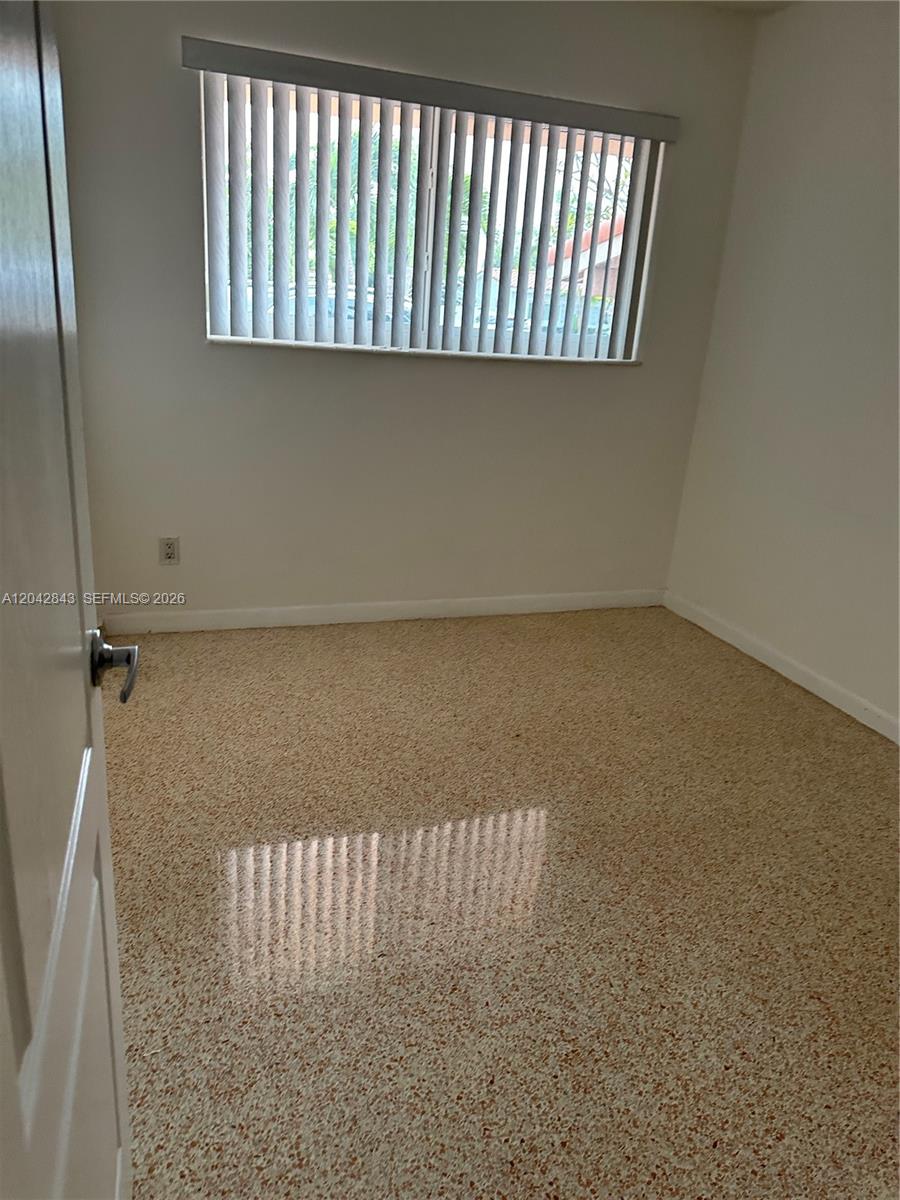 An empty room features light-colored walls, a window with vertical blinds, and speckled flooring — 7931 SW 13th Ter # 7931, Miami FL 33144, MIAMI, FL