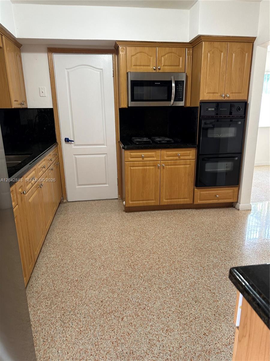 A kitchen features light wood cabinets, black countertops, a double oven, and speckled flooring — 7931 SW 13th Ter # 7931, Miami FL 33144, MIAMI, FL