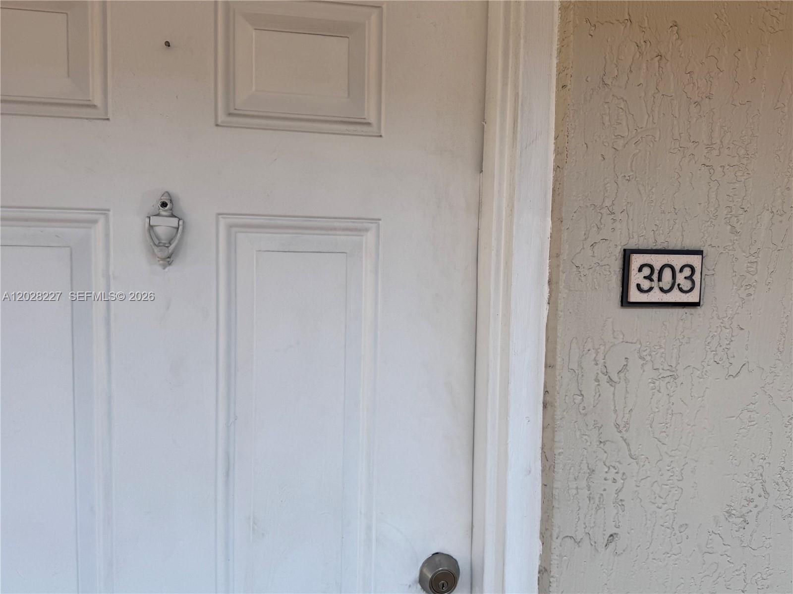 A white front door with a door knocker and a unit number sign 303 — 6195 NW 186th St # 303, Hialeah FL 33015, HIALEAH, FL