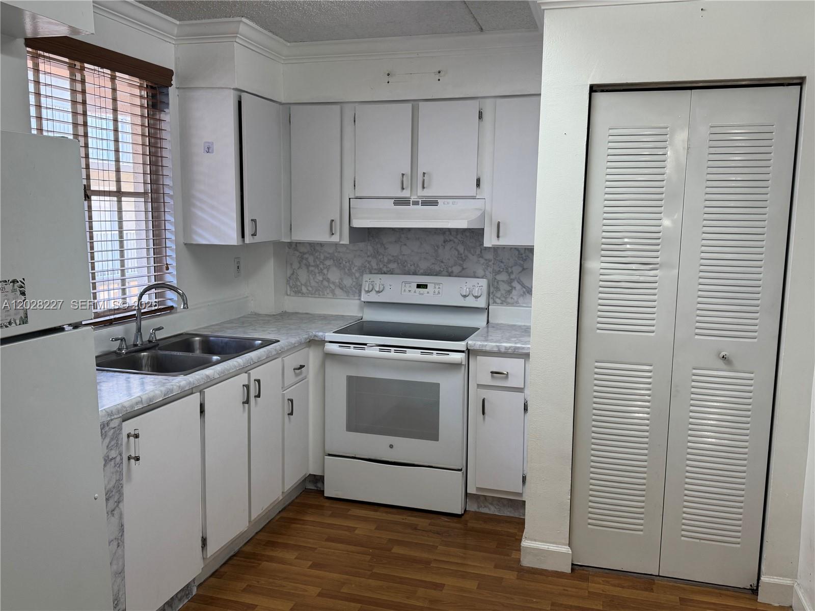 A kitchen features white cabinets, a white stove, a double sink, and wood-look flooring — 6195 NW 186th St # 303, Hialeah FL 33015, HIALEAH, FL
