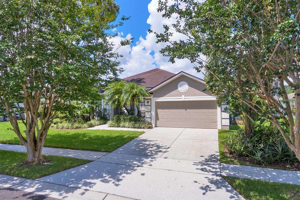 A single-story suburban house with a tan exterior, a two-car garage, and a concrete driveway — 13903 BLUEWATER CIRCLE, ORLANDO, FL