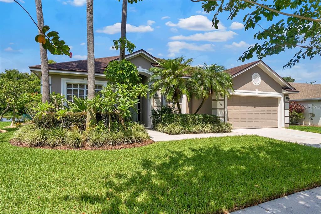 A single-story house with a tan exterior, a two-car garage, and lush tropical landscaping — 13903 BLUEWATER CIRCLE, ORLANDO, FL