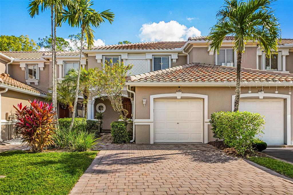 A two-story townhouse with a brick paver driveway, two garage doors, and palm trees — 3345 ANTICA STREET, FORT MYERS, FL