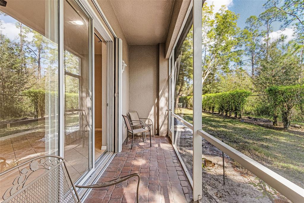 A screened-in patio features brick pavers, two chairs, and a view of a wooded yard — 3345 ANTICA STREET, FORT MYERS, FL