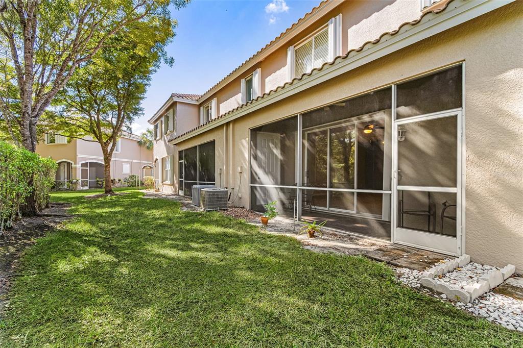 A view of a tan two-story townhouse exterior with a screened-in patio and grassy yard — 3345 ANTICA STREET, FORT MYERS, FL