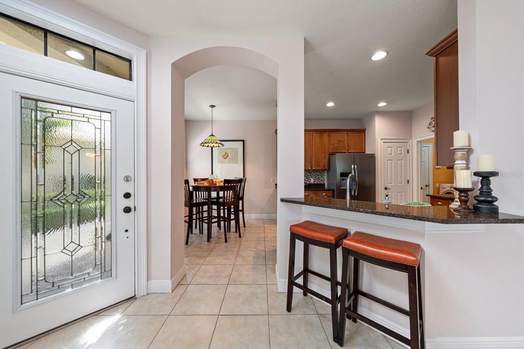 A kitchen with a breakfast bar and stools opens into a dining area with tile floors — 8241 ACADIAN LANE, SEMINOLE, FL