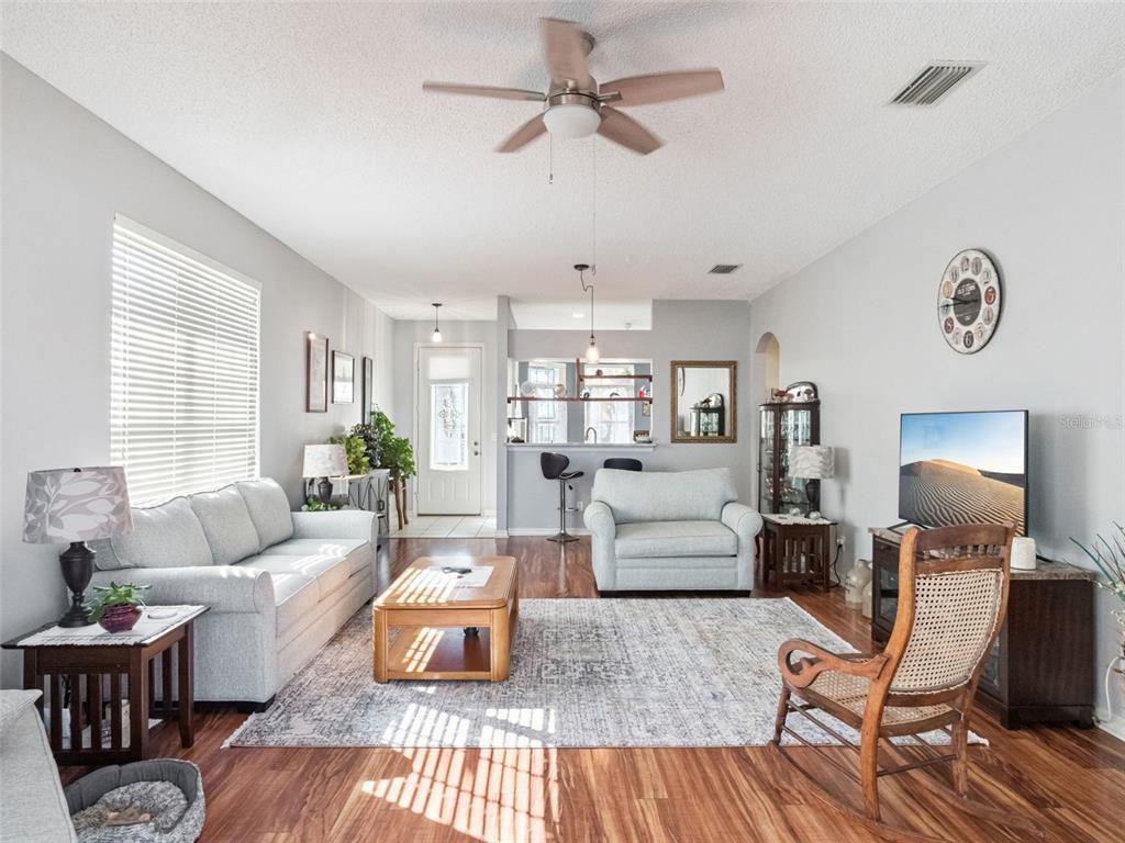 A living room features light gray walls, wood-look flooring, a ceiling fan, and a kitchen pass-through — 4921 GLEN COE STREET, LEESBURG, FL
