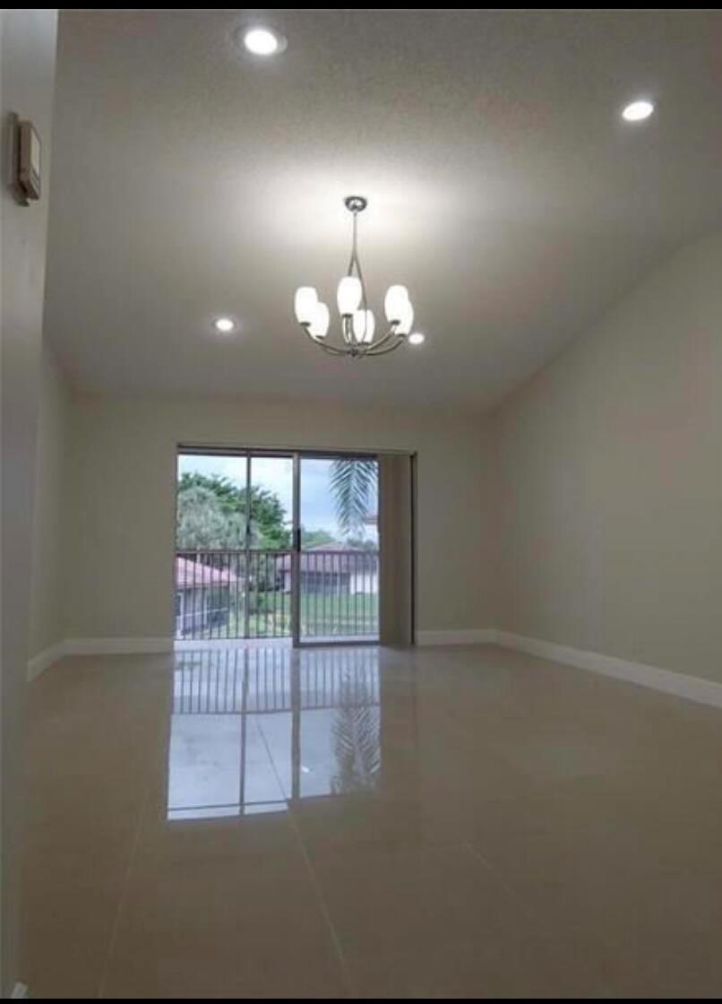An empty room with light-colored tile flooring, a chandelier, recessed lighting, and a sliding glass door — 9903 Three Lakes Circle, Boca Raton FL 33428, BOCA RATON, FL