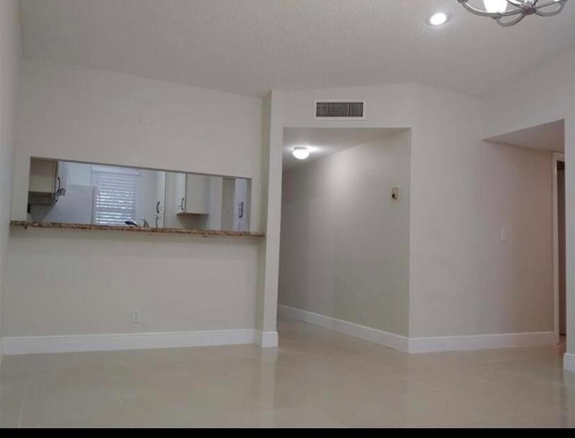 A living area with light tile floors, a kitchen pass-through window, and a hallway entrance — 9903 Three Lakes Circle, Boca Raton FL 33428, BOCA RATON, FL
