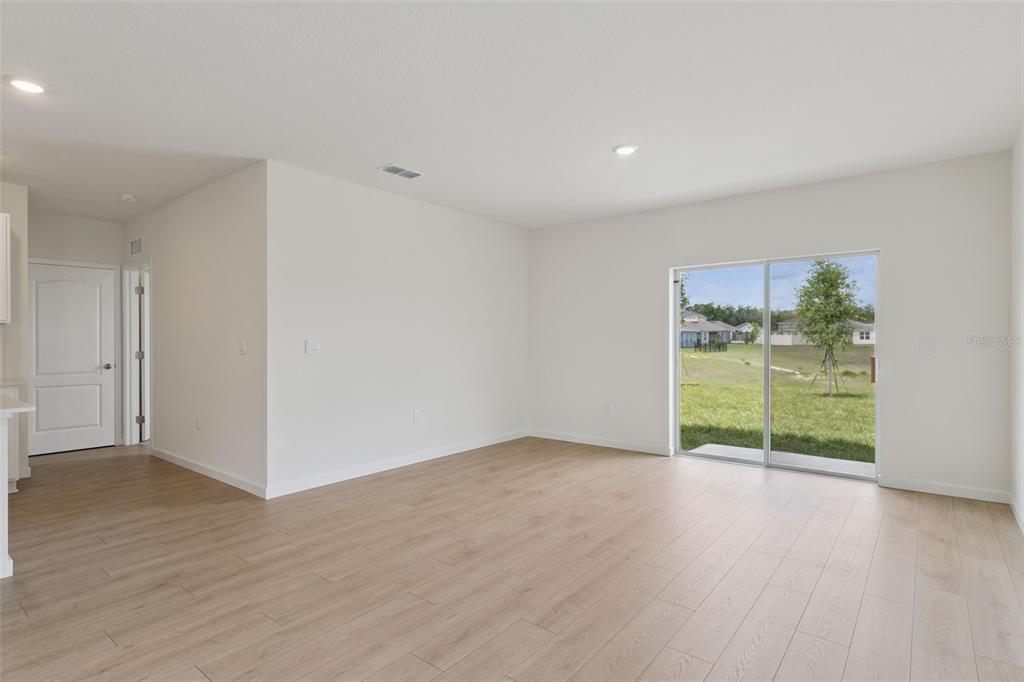 An empty room with light wood-look flooring, white walls, and a sliding glass door — 917 5TH STREET, PORT ORANGE, FL