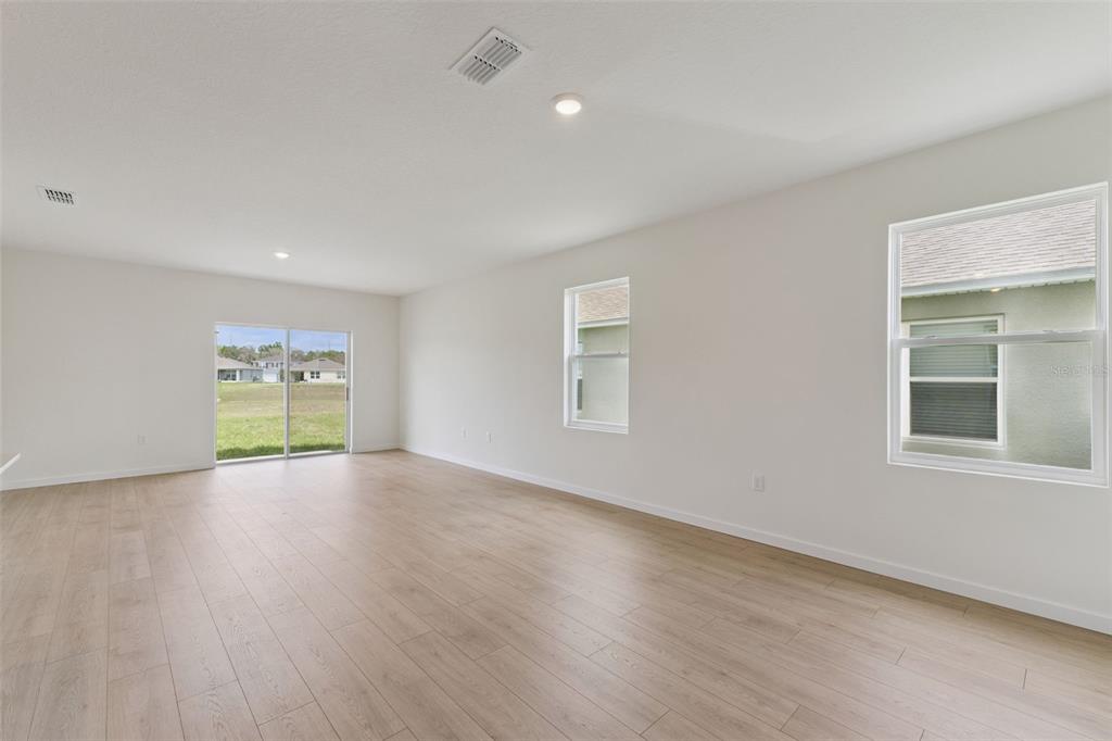 An empty room with light wood-look flooring, white walls, a sliding glass door, and windows — 917 5TH STREET, PORT ORANGE, FL
