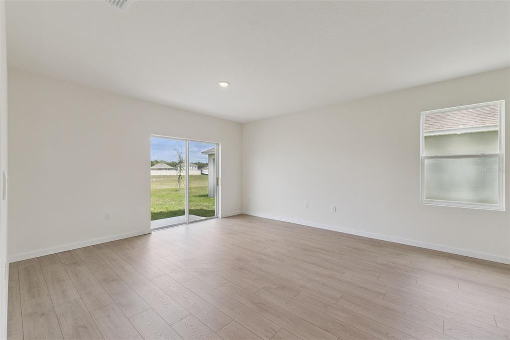 An empty room with light wood-look flooring, white walls, a sliding glass door, and window — 917 5TH STREET, PORT ORANGE, FL