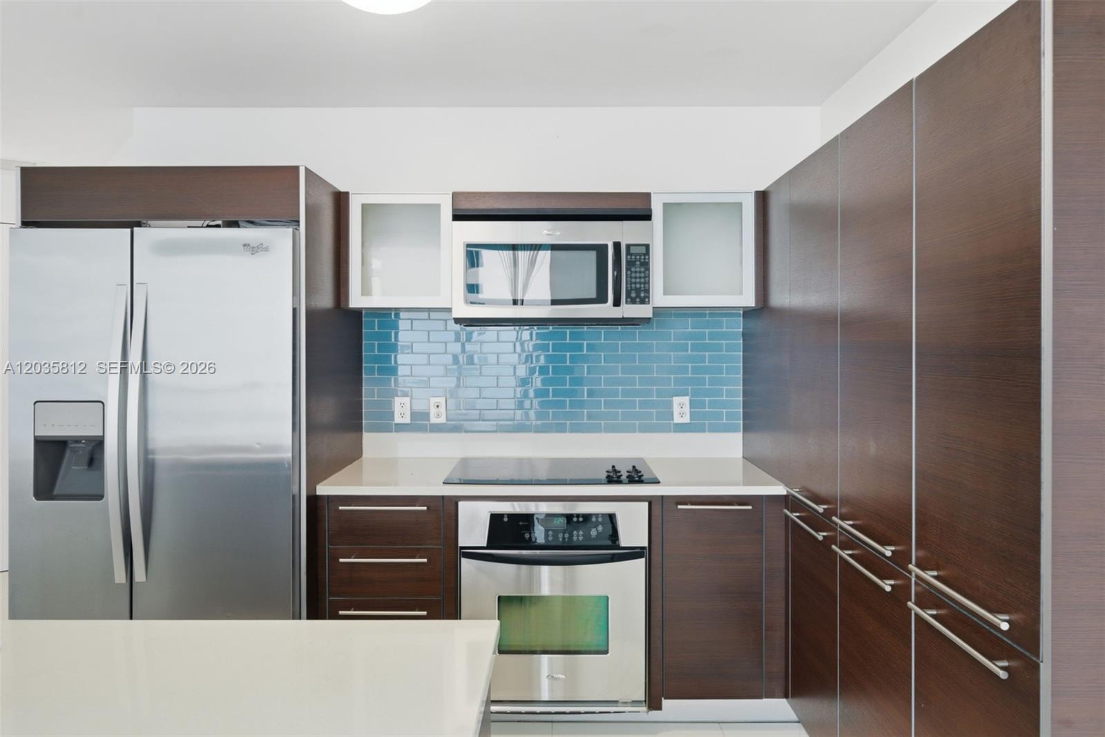 A modern kitchen features dark wood cabinetry, stainless steel appliances, and a blue tiled backsplash — 1900 N Bayshore Dr # 2207, Miami FL 33132, MIAMI, FL