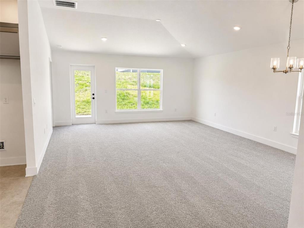 A spacious, carpeted living area features white walls, recessed lighting, a glass door, and windows — 1631 ANN ROSE WAY, LEESBURG, FL