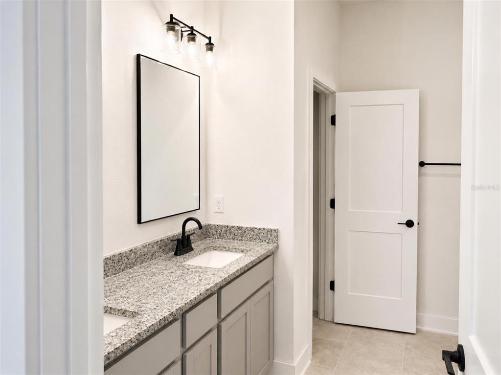 A bathroom features a gray vanity with a granite countertop, a black-framed mirror, and lighting — 1631 ANN ROSE WAY, LEESBURG, FL