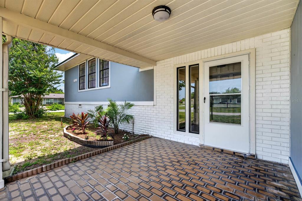 A covered entryway with a brick-paved floor, white brick wall, and a glass-paneled front door — 600 SEA GULL COURT, EDGEWATER, FL