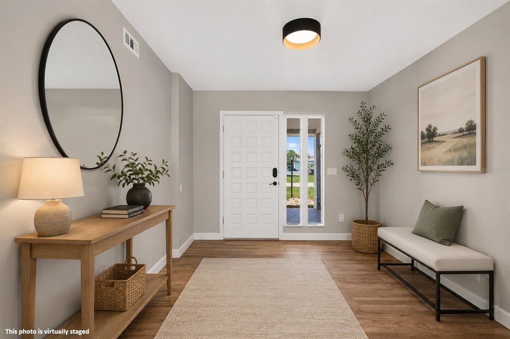 This is a virtually staged entryway featuring a console table, bench, mirror, and wood flooring — 600 SEA GULL COURT, EDGEWATER, FL