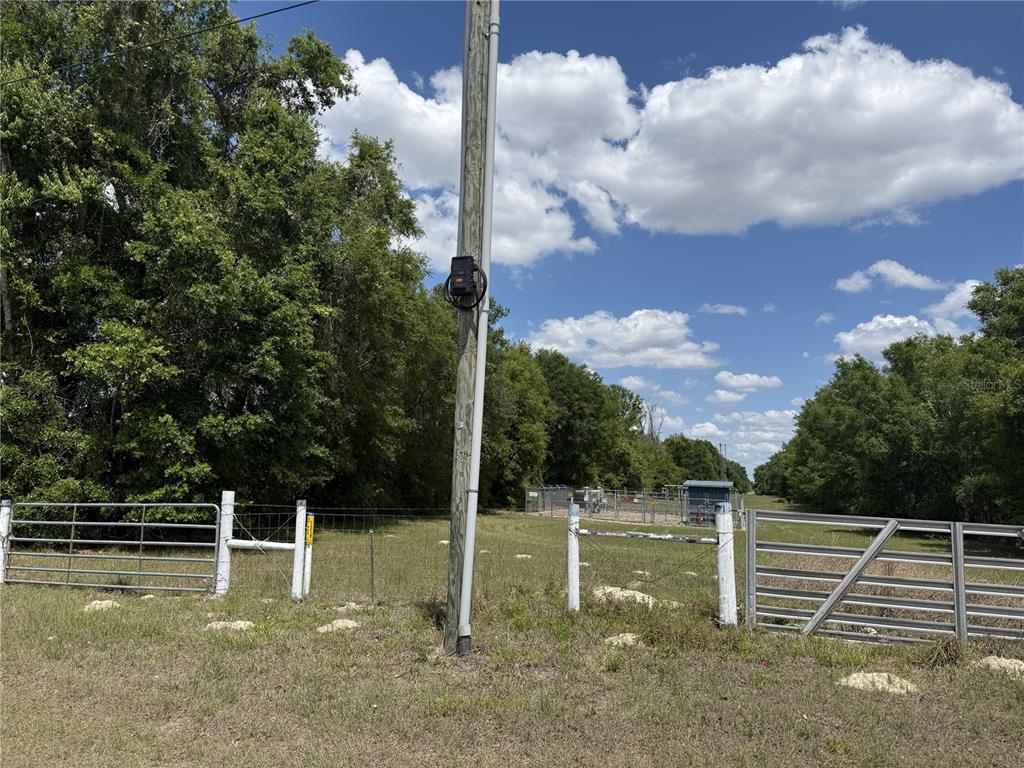 A utility pole stands in a grassy field next to a metal gate and fence — 0 NW 140TH STREET, CHIEFLAND, FL