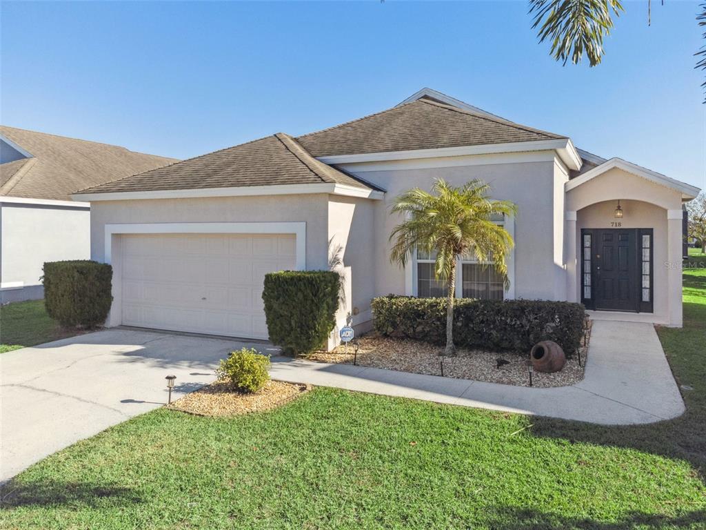 A single-story house with a beige stucco exterior, a two-car garage, and a palm tree — 718 CORVINA DRIVE, DAVENPORT, FL