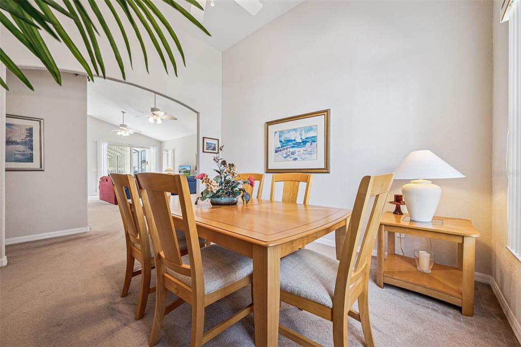 A dining room features a wooden table and chairs on carpeted flooring under a vaulted ceiling — 718 CORVINA DRIVE, DAVENPORT, FL