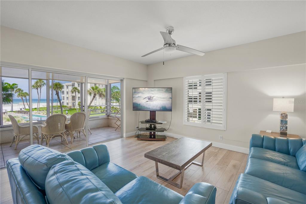 A living room with blue leather sofas, a television, and a balcony overlooking the ocean — 6146 MIDNIGHT PASS ROAD UNIT 12S, SARASOTA, FL