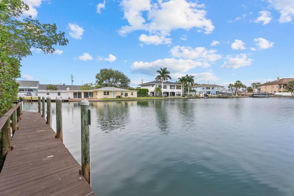 A wooden dock extends into a calm canal lined with waterfront houses and palm trees — 101 LOUELLA LANE UNIT 10, NOKOMIS, FL