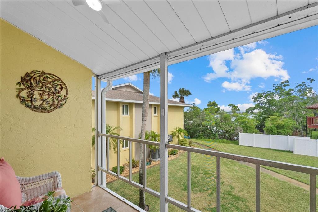 A screened-in balcony overlooks a grassy yard, a neighboring building, and a distant lake — 101 LOUELLA LANE UNIT 10, NOKOMIS, FL