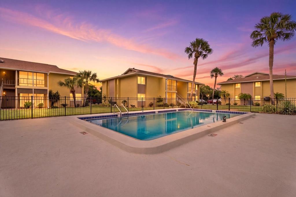 A swimming pool sits in front of multi-story apartment buildings under a sunset sky — 101 LOUELLA LANE UNIT 10, NOKOMIS, FL