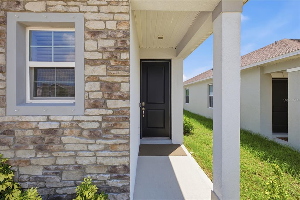 The exterior view shows a stone-accented house facade with a covered entryway and black door — 3963 SAGEFIELD DRIVE, HARMONY, FL