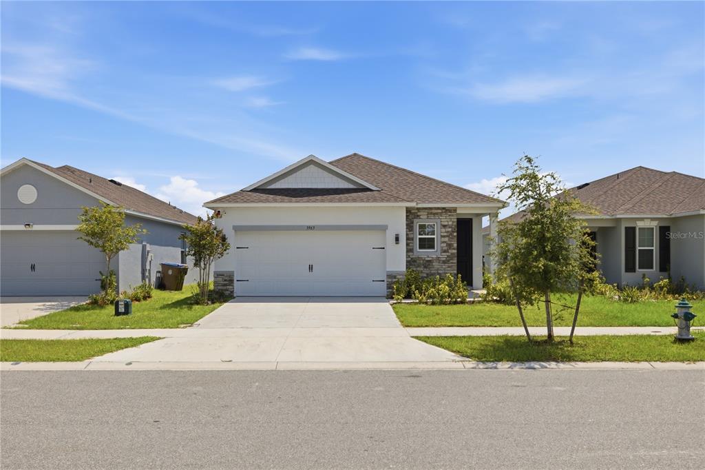 A single-story suburban house with a two-car garage, stone facade accents, and a concrete driveway — 3963 SAGEFIELD DRIVE, HARMONY, FL