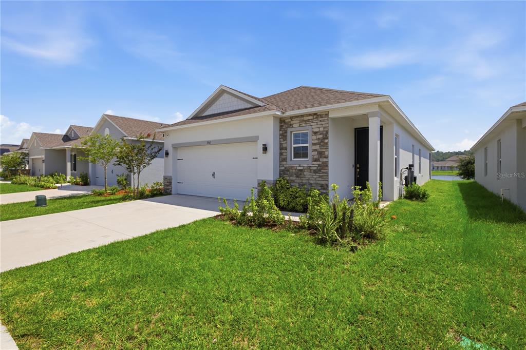 A single-story suburban house with a white exterior, stone accents, and a two-car garage — 3963 SAGEFIELD DRIVE, HARMONY, FL