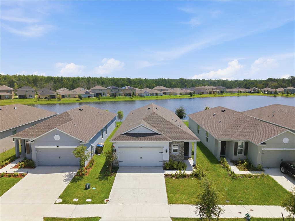 An aerial view shows three suburban houses with gray roofs facing a lake — 3963 SAGEFIELD DRIVE, HARMONY, FL