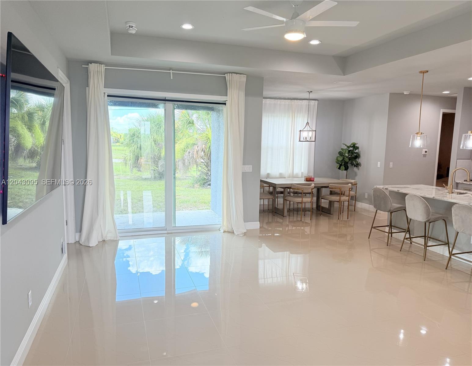 A bright open-concept living and dining area features tile floors, a sliding glass door, and kitchen — 106 Plantation Dr, La Belle FL 33935, LA BELLE, FL