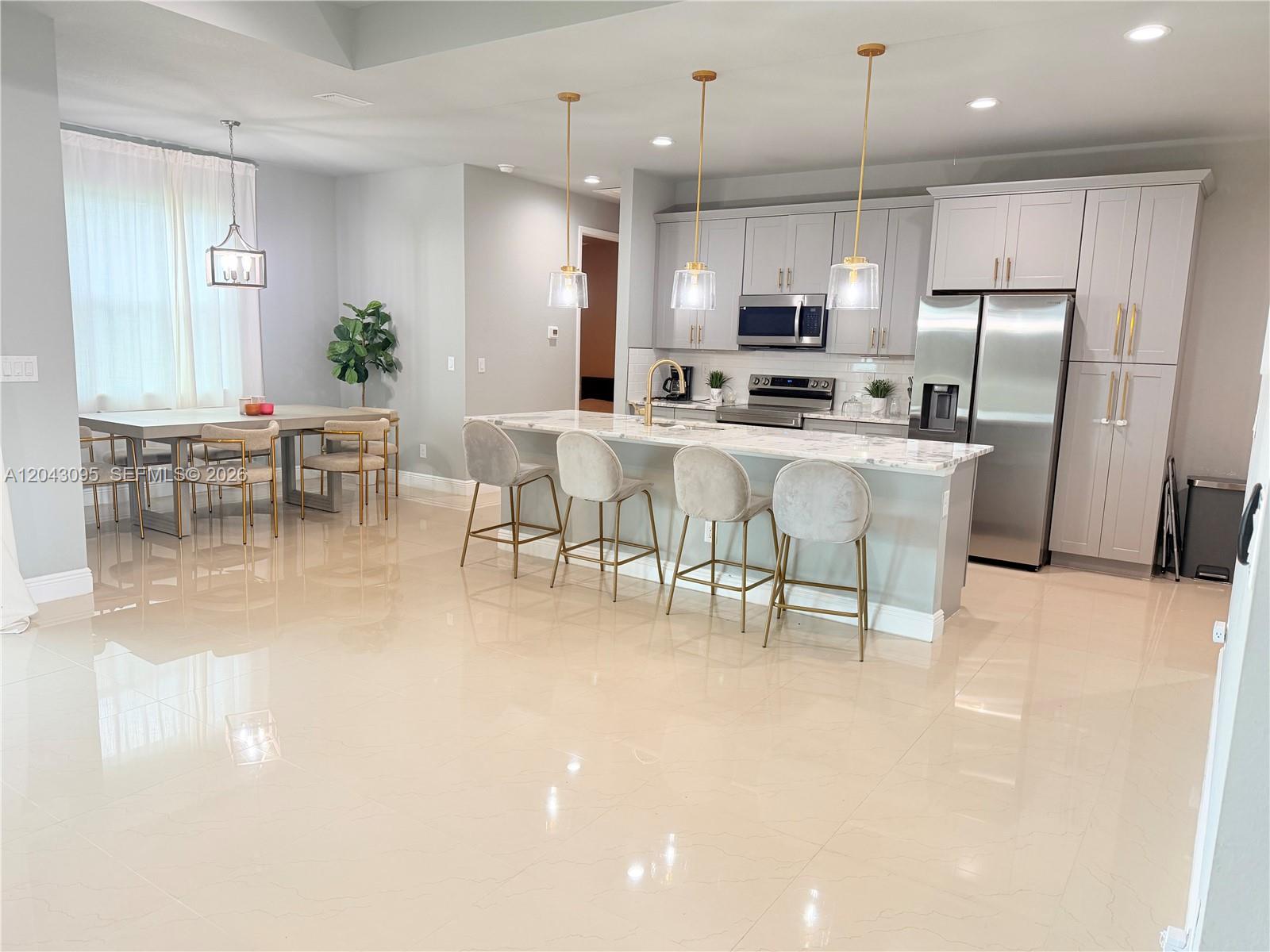 A modern kitchen features light gray cabinetry, a marble-topped island, and four upholstered bar stools — 106 Plantation Dr, La Belle FL 33935, LA BELLE, FL
